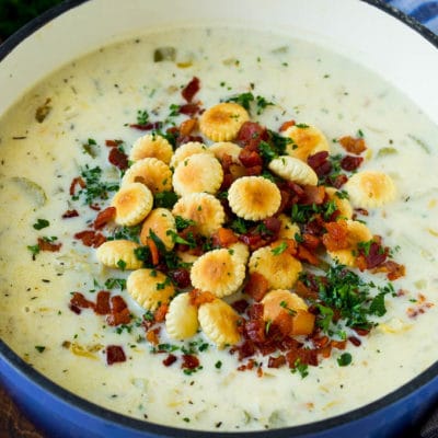 A pot of New England clam chowder topped with oyster crackers, bacon and parsley.