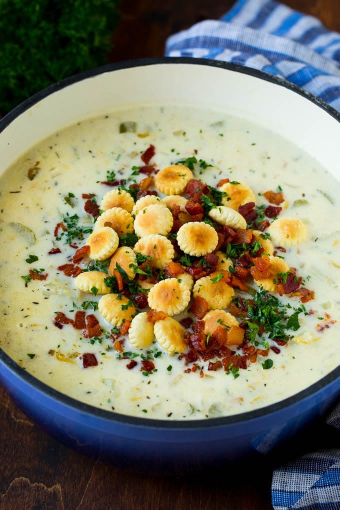 A pot of New England clam chowder topped with oyster crackers, bacon and parsley.