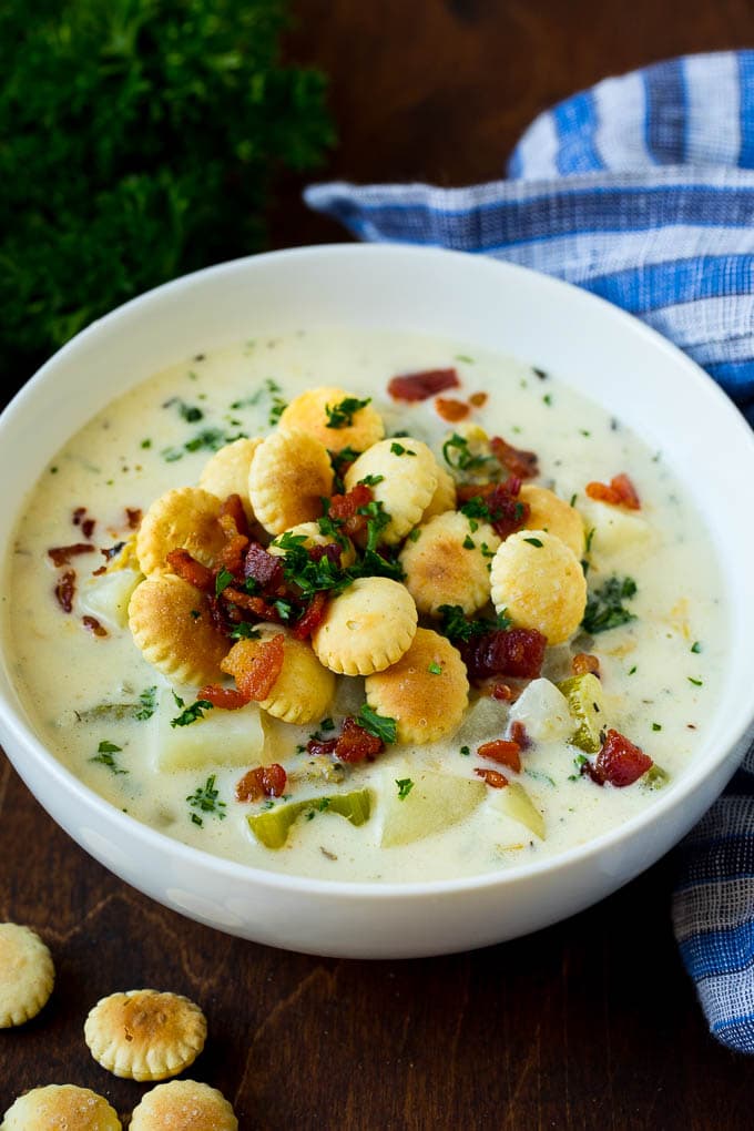 A bowl of New England clam chowder topped with bacon and crackers.