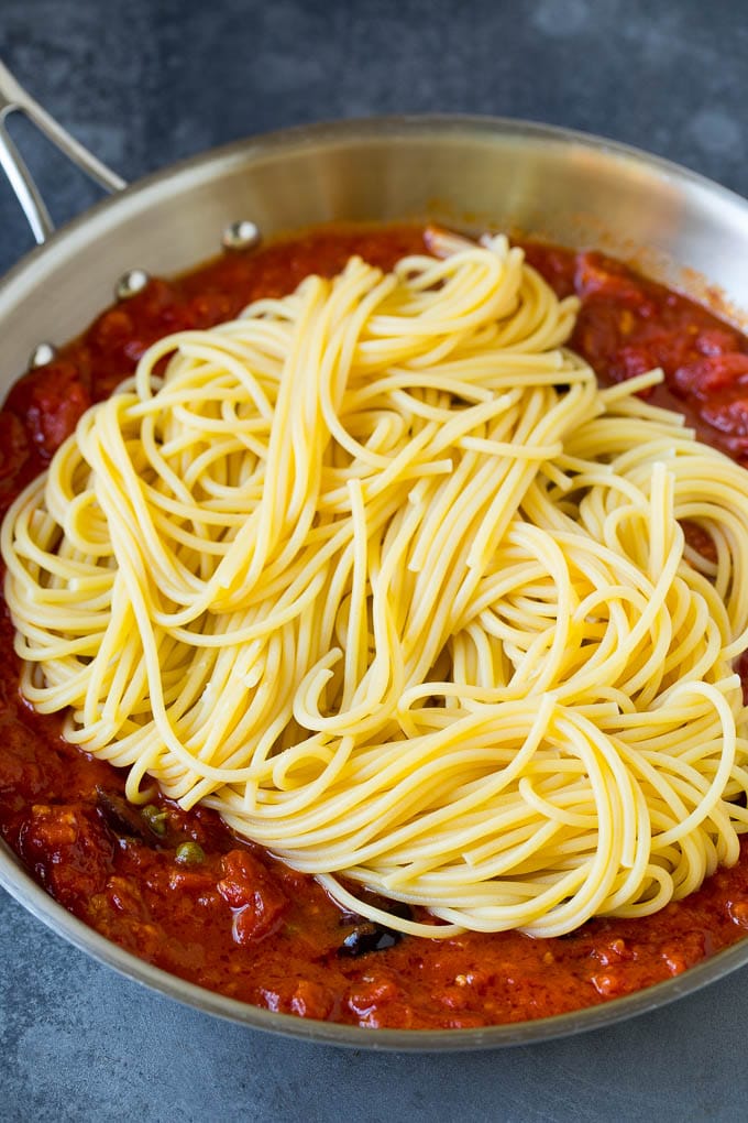 Spaghetti in a pan of tomato sauce with olives and capers.