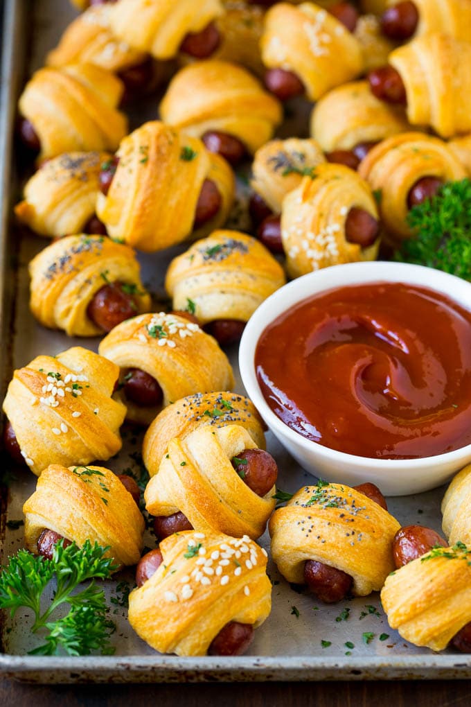 A sheet pan of pigs in a blanket, garnished with parsley and served with ketchup.