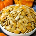 A bowl of roasted pumpkin seeds surrounded by pumpkins and gourds.