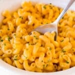 Slow cooker mac and cheese topped with parsley, with a serving spoon in it.