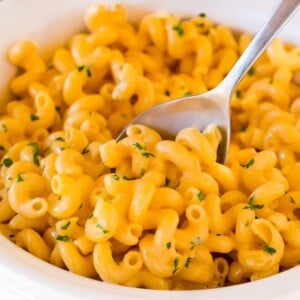 Slow cooker mac and cheese topped with parsley, with a serving spoon in it.