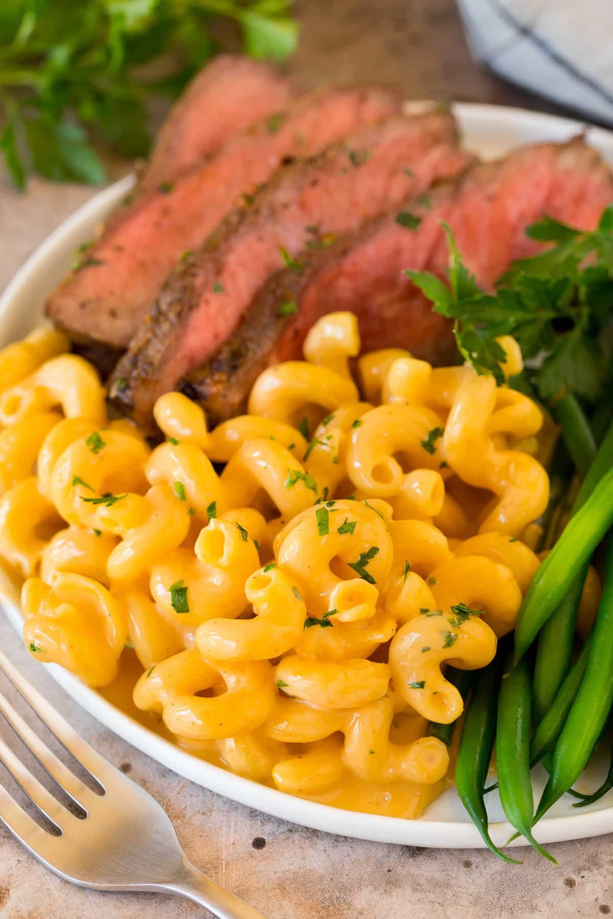 Slow cooker mac and cheese on a plate with sliced steak and vegetables.