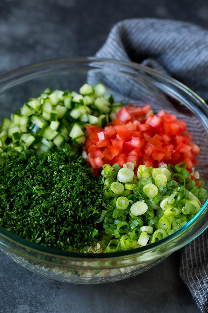 A bowl of bulgur topped with herbs, tomatoes and cucumber.