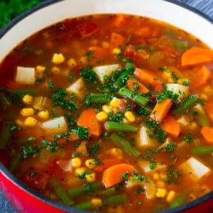 A pot of vegetable soup filled with colorful veggies, potatoes and herbs.