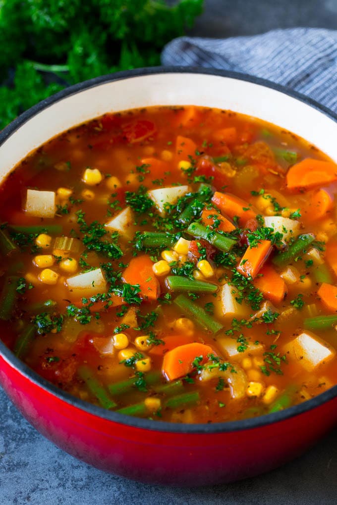 A pot of vegetable soup filled with colorful veggies, potatoes and herbs.