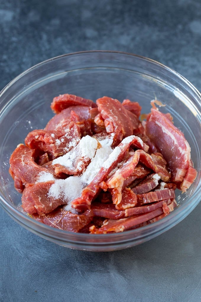 Sliced flank steak and cornstarch in a bowl.