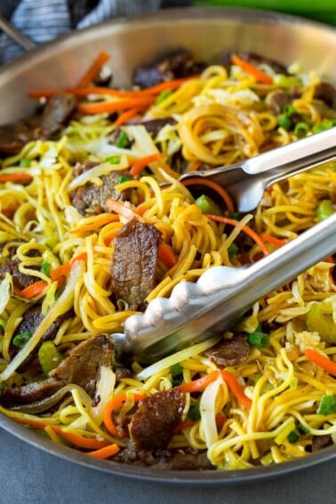 Tongs serving up a portion of beef chow mein.