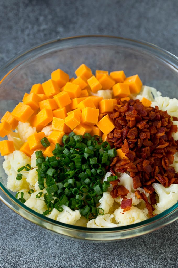 A bowl of cauliflower with bacon, cheese and green onions on top.