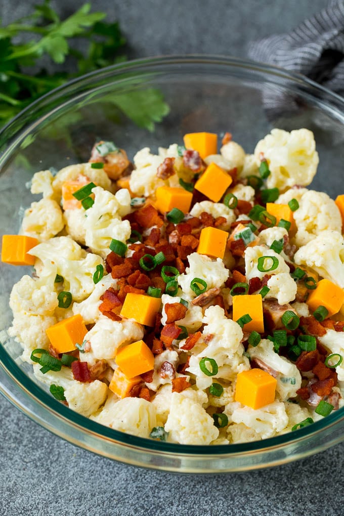 A bowl of cauliflower salad garnished with bacon and green onions.