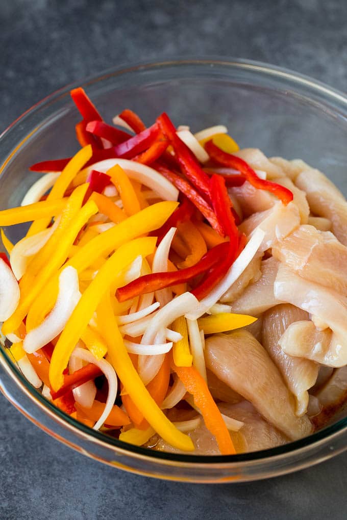 Chicken breasts and peppers in a bowl of marinade.