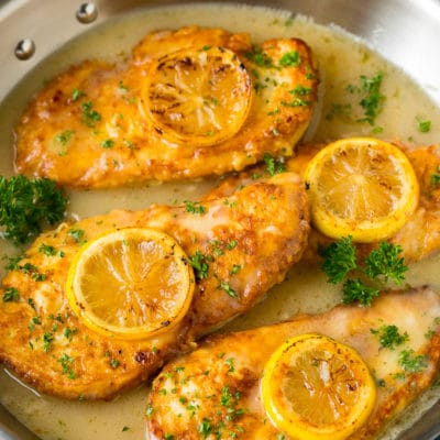 Chicken francese in a white wine sauce, garnished with lemon slices.