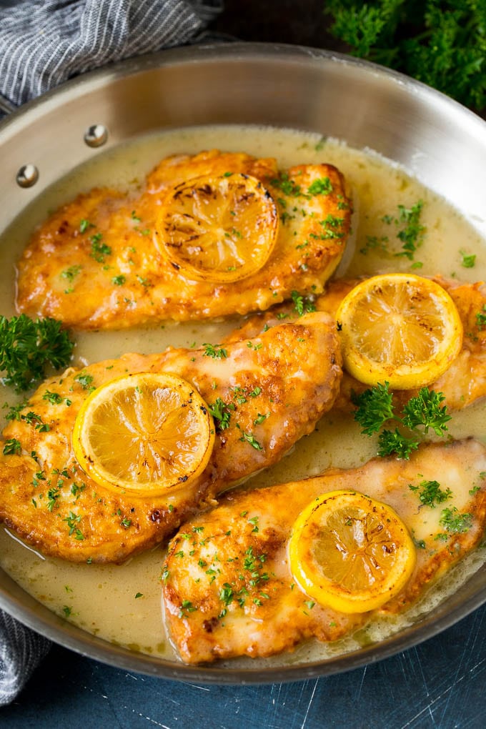 Chicken francese in a white wine sauce, garnished with lemon slices.