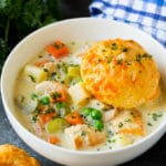 A bowl of chicken pot pie soup with a biscuit on top.