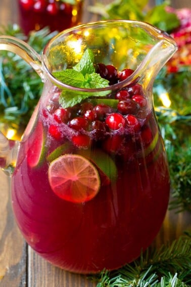 A pitcher of christmas punch garnished with cranberries and mint.