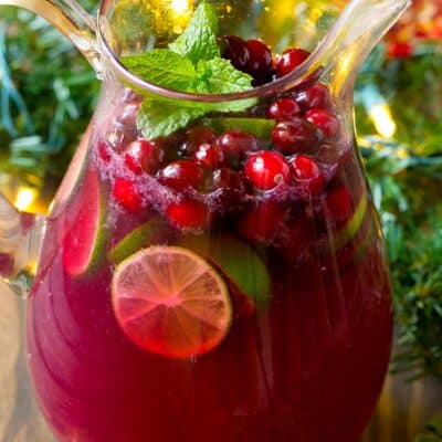 A pitcher of christmas punch garnished with cranberries and mint.