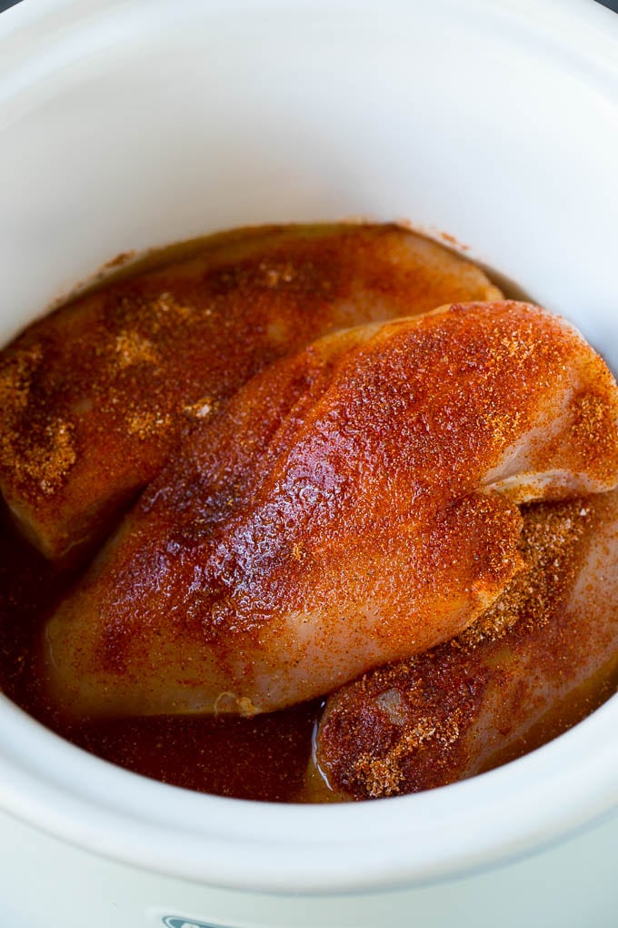 A slow cooker full of seasoned chicken breasts and chicken broth.