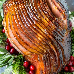 A glazed ham on a platter with herbs and cranberries.