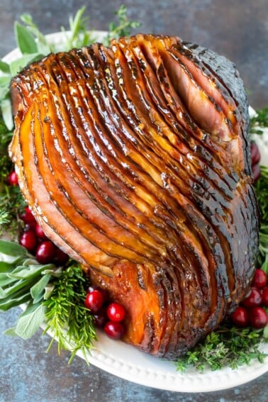 A glazed ham on a platter with herbs and cranberries.