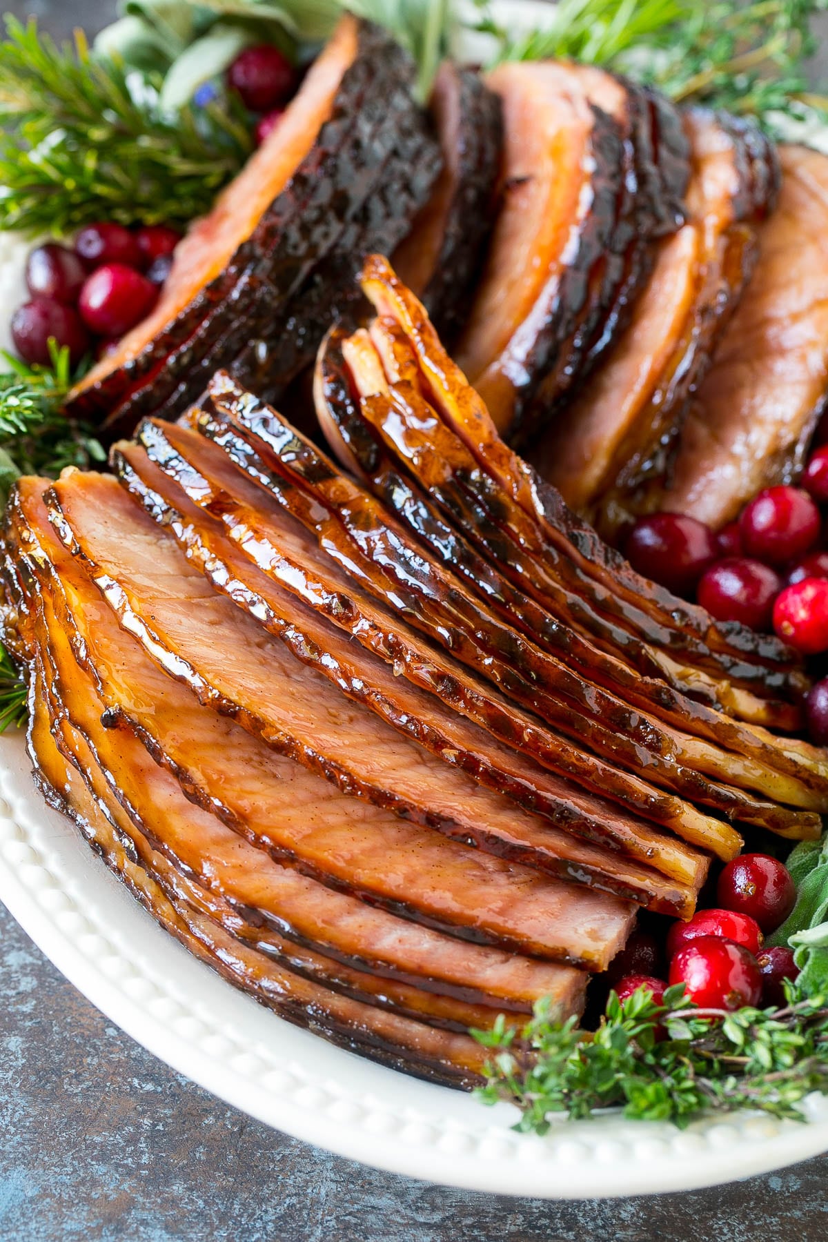 Sliced glazed ham on a serving plate with a garnish of berries and herbs.