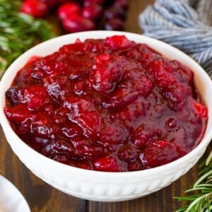A bowl of homemade cranberry sauce with a serving spoon and garnishes.
