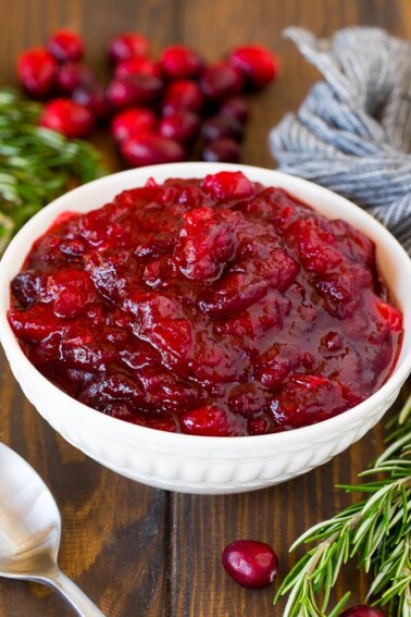 A bowl of homemade cranberry sauce with a serving spoon and garnishes.
