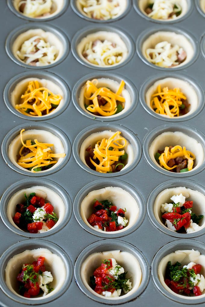 Muffin tins filled with pie crust, vegetables, meat and shredded cheese.