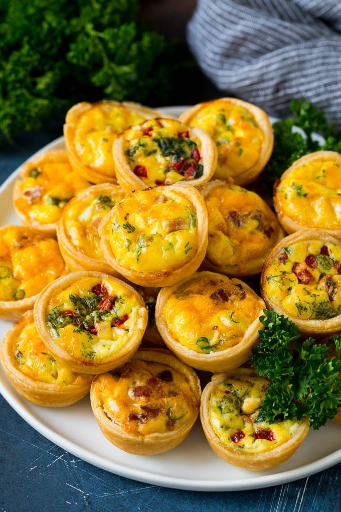 A plate of mini quiche filled with meats, vegetables and cheeses.