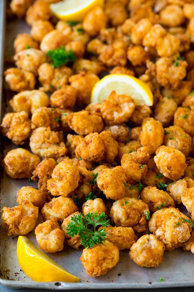 Popcorn shrimp on a sheet pan, garnished with lemon and parsley.