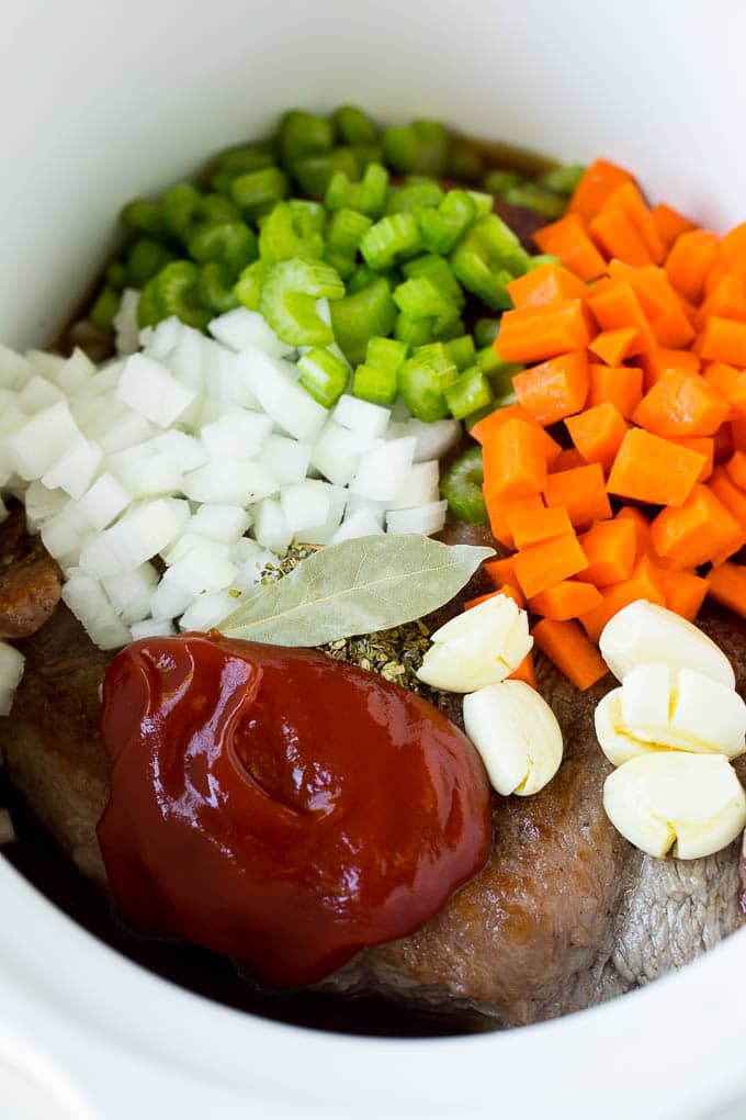 Brisket, vegetables, herbs and seasonings in a slow cooker.