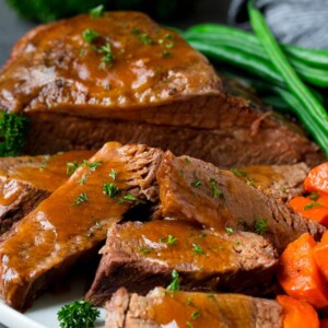 Slow cooker brisket sliced and topped with sauce, served with vegetables.