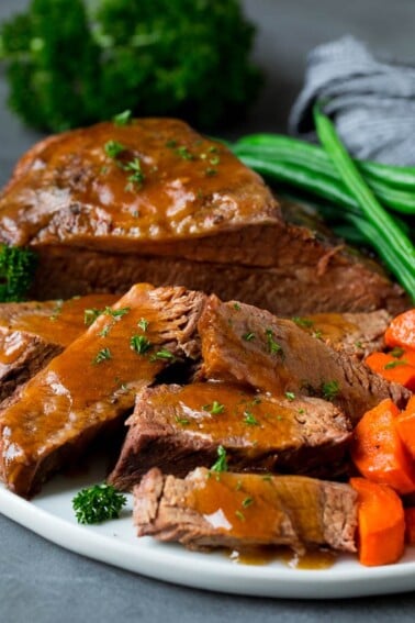 Slow cooker brisket sliced and topped with sauce, served with vegetables.