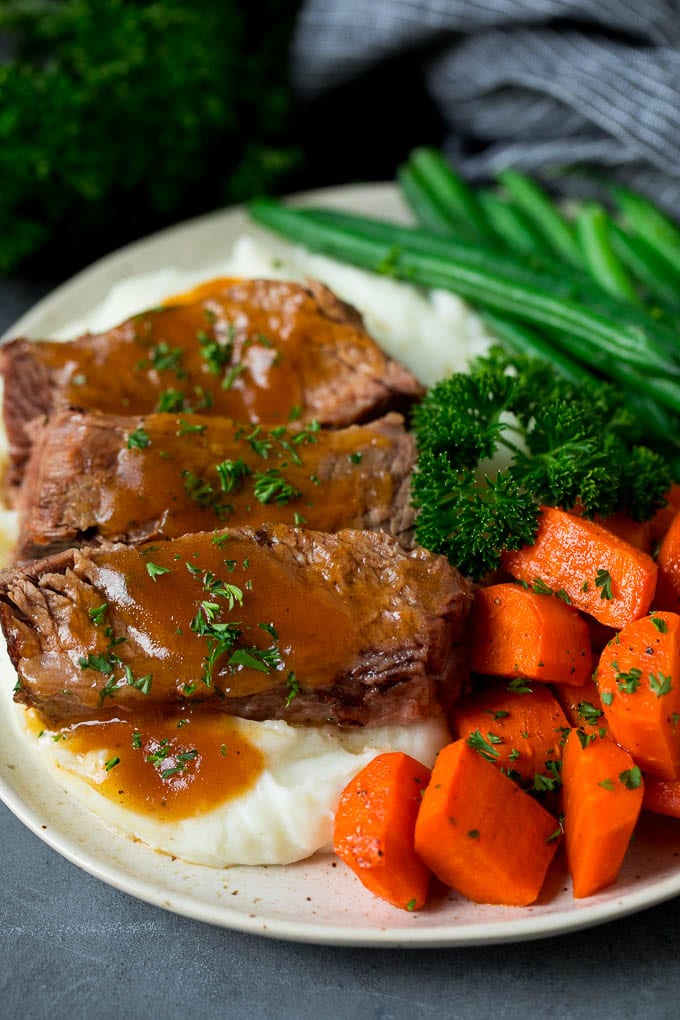 Slow cooker brisket served over mashed potatoes with vegetables on the side.