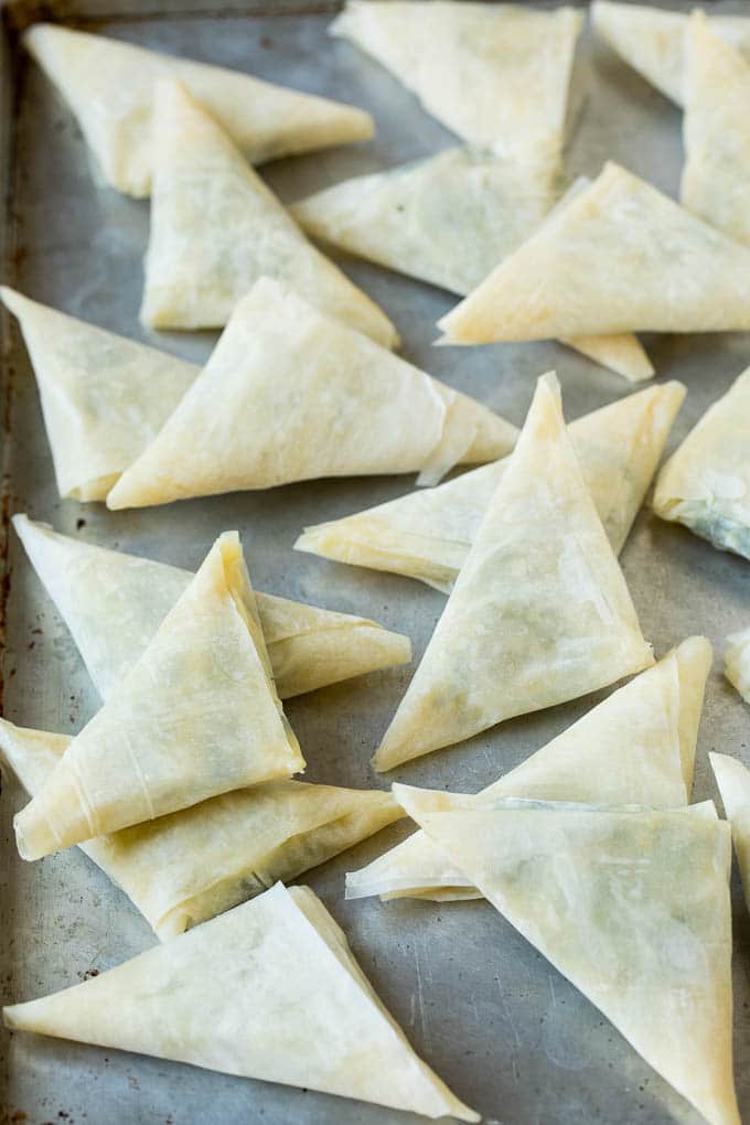 Folded stuffed phyllo triangles on a sheet pan.