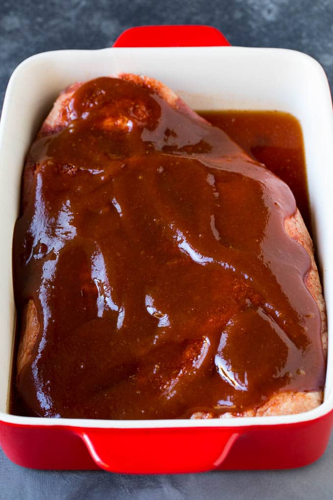 Beef in a baking dish coated with spices and BBQ sauce.