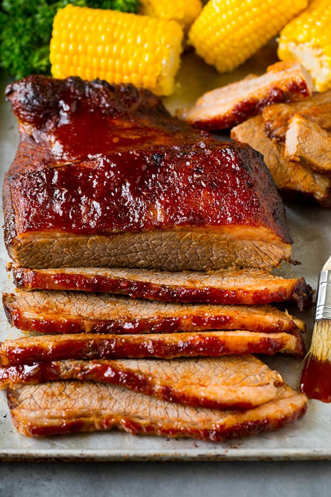 An oven baked beef brisket cut into slices and served alongside corn on the cob.