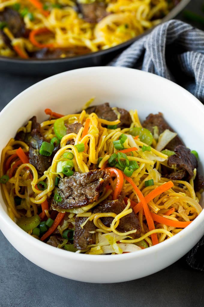 A bowl of beef chow mein topped with sliced green onions.