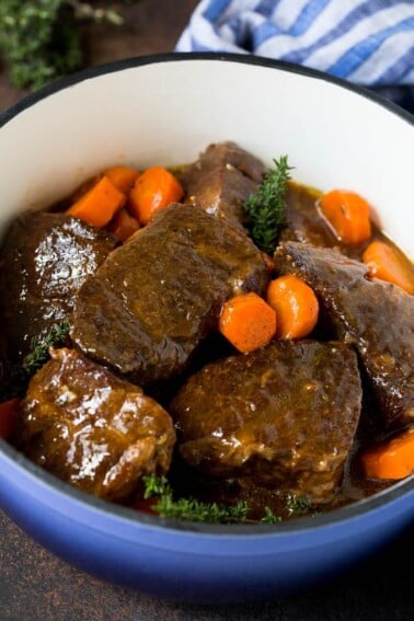 Braised short ribs with carrots in a blue pot, garnished with fresh thyme.