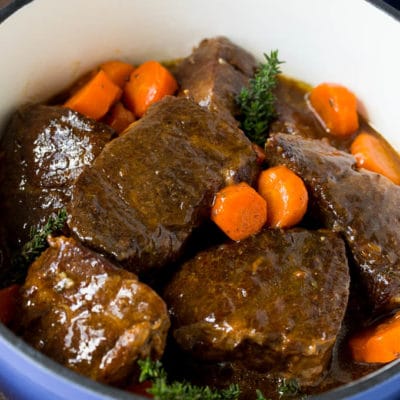 Braised short ribs with carrots in a blue pot, garnished with fresh thyme.
