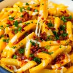 A skillet of cheese fries with bacon, and a hand reaching for one.