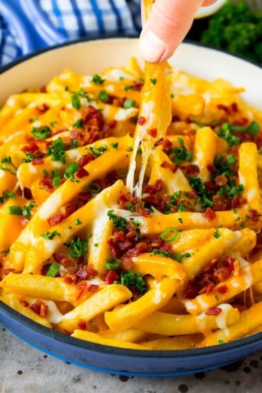 A skillet of cheese fries with bacon, and a hand reaching for one.