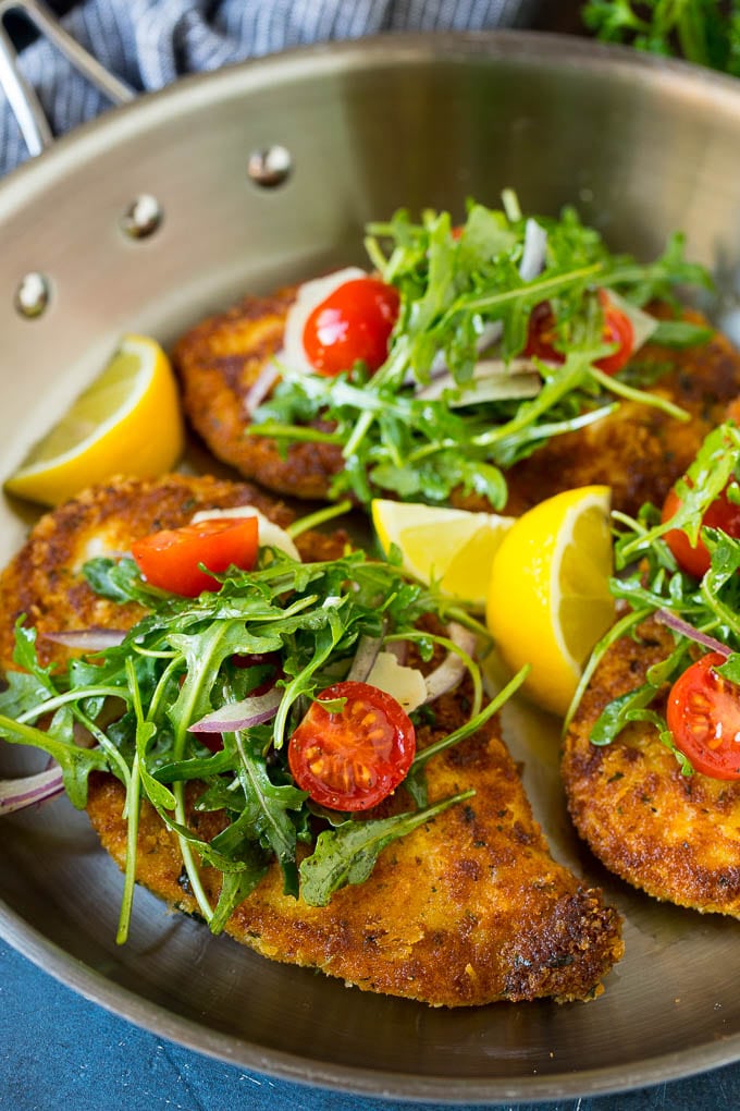 Chicken milanese topped with arugula salad in a skillet.