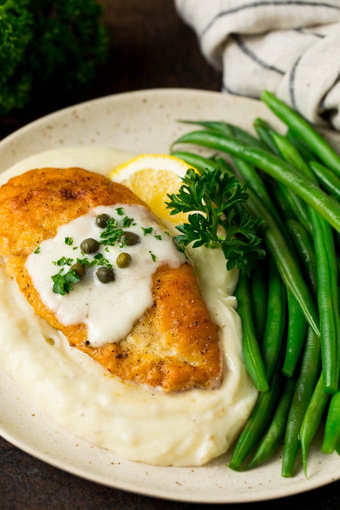 Chicken scallopini served over mashed potatoes with a side of green beans.