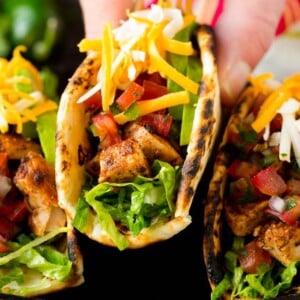 A hand picking up a chicken taco stuffed with meat, cheese and salsa.