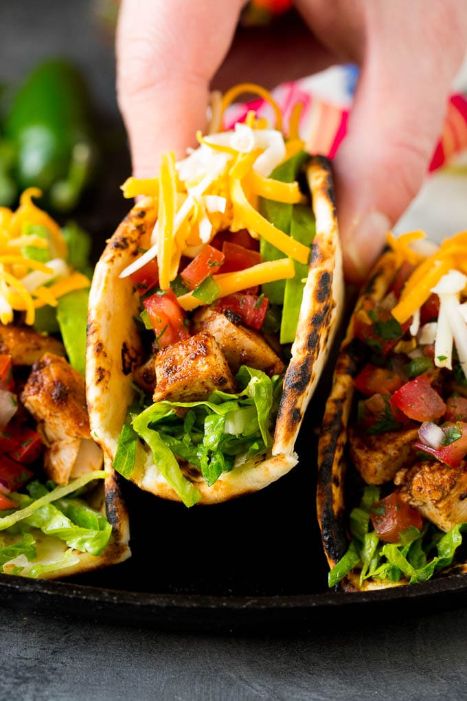 A hand picking up a chicken taco stuffed with meat, cheese and salsa.