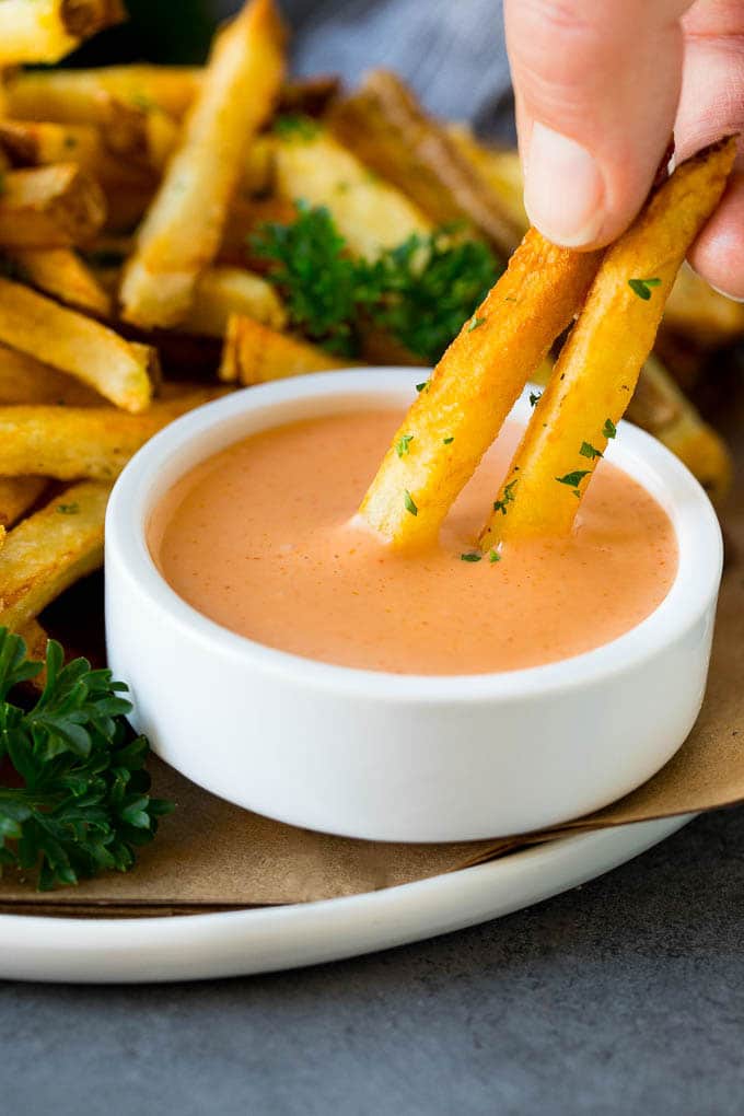 A hand dipping french fries into fry sauce.