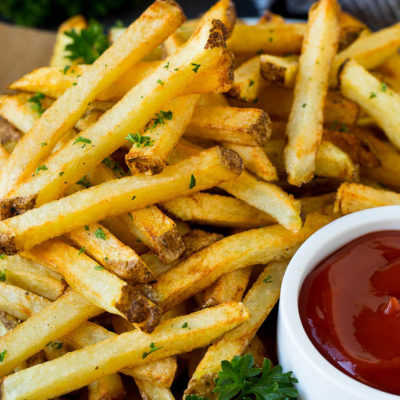 A plate of homemade french fries served with a bowl of ketchup.
