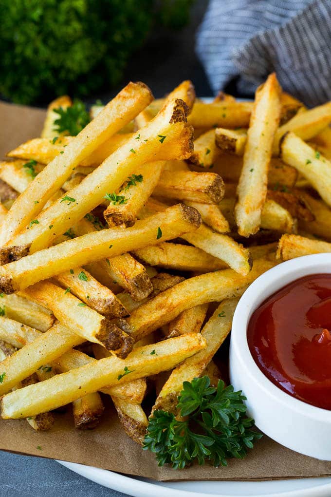 A plate of homemade french fries served with a bowl of ketchup.